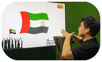 Guest playing Drum-to-Reveal interactive game at a Dubai event, beating the drum to reveal a hidden image on a large screen, designed for exhibitions and activations.